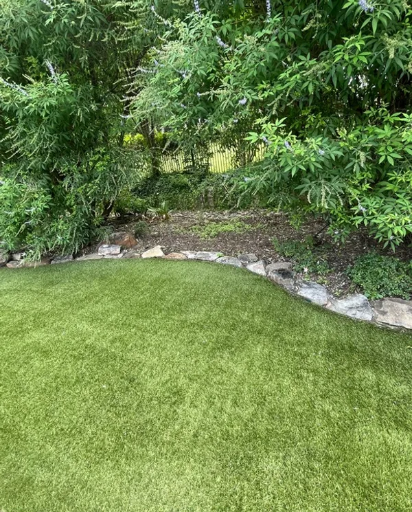 Beautiful artificial turf lawn with stone border after professional grooming